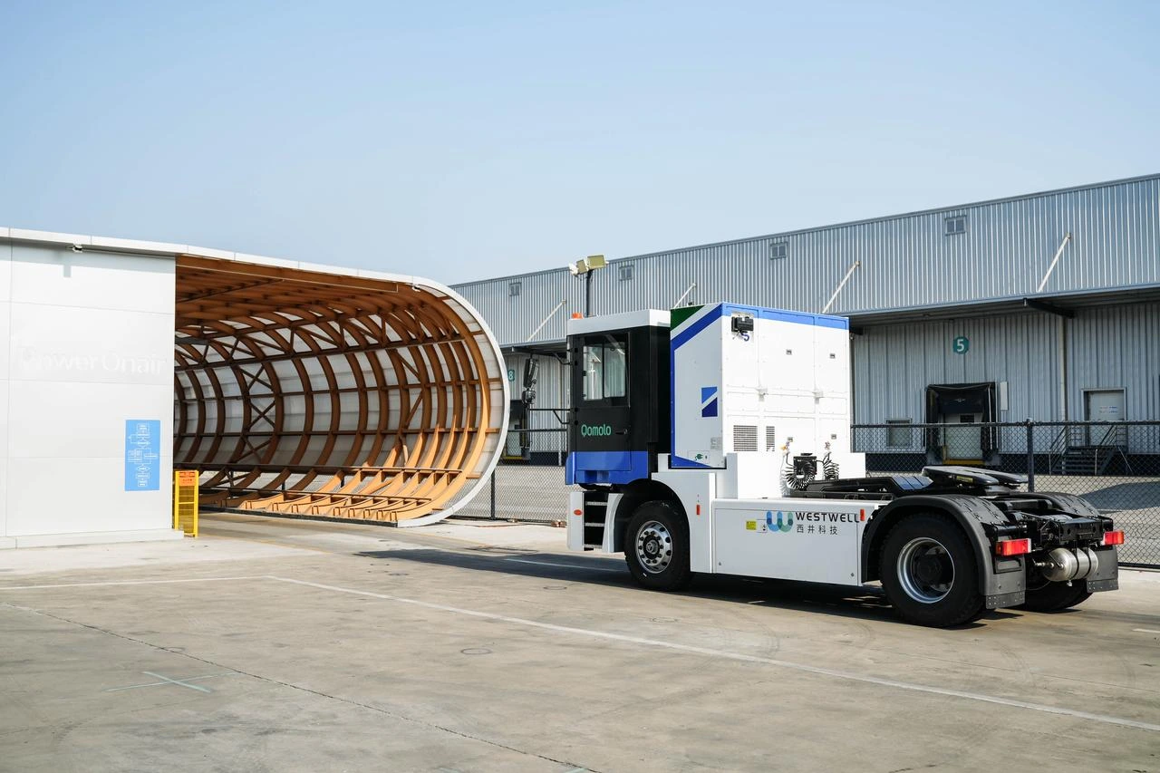 Westwell Qomolo electric tractor displayed near PowerOnair battery-swapping infrastructure at an industrial facility.